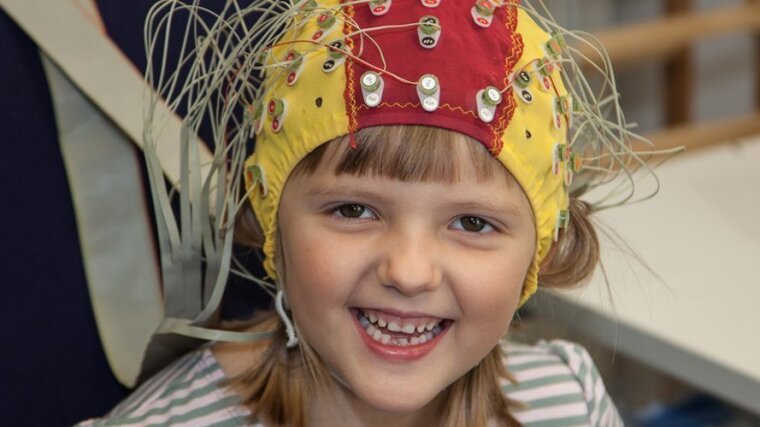 Child wearing EEG hood laughs into the camera